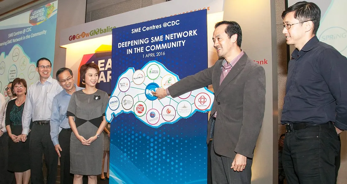 Event attendees stand near a signboard that reads "Deepening SME Network in the Community" dated 1 April 2016.